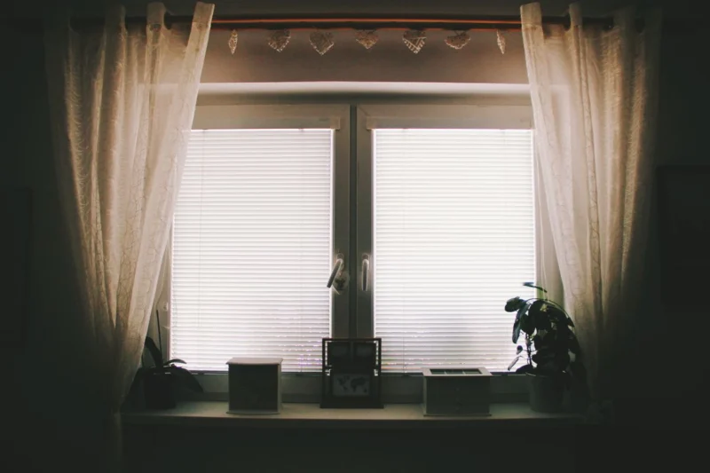 Window with pale blinds and sheer curtains in evening light