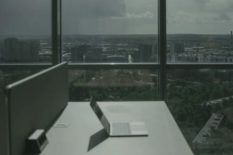 Laptop on an office desk beside floor-to-ceiling windows