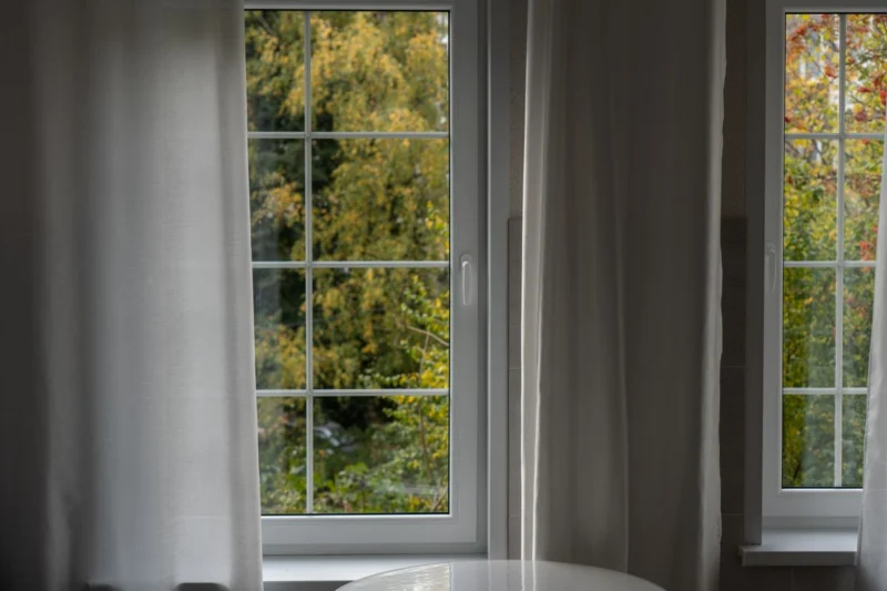 Tall white-framed window with grey curtains and a garden view